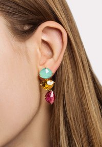 Tre orecchini a goccia che presentano un gemma triangolare verde menta, una gemma gialla sfaccettata e una gemma rosa a forma di marquise, montati in metallo dorato.