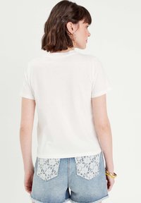 White cotton t-shirt with short sleeves, paired with light blue denim shorts featuring lace detail on the back pockets. Smooth texture.