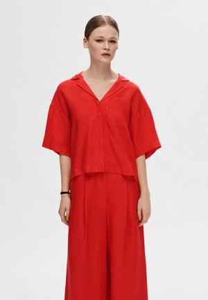 Blusa roja de manga corta con un corte suelto, escote en V y bolsillo en el pecho, combinada con pantalones de pierna ancha a juego, confeccionados en tejido ligero.