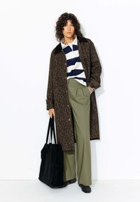 Manteau à imprimé léopard, polo rayé bleu marine et blanc, pantalon vert olive, sac fourre-tout noir, chaussures noires à clous, détails en tissu texturé.