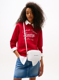 Sudadera roja con texto blanco, superpuesta a una camisa blanca con cuello, combinada con una falda de mezclilla. Bolso cruzado blanco con logo.