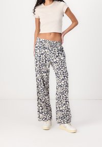 Bloomende wijde broek met een patroon in marineblauw en crème, voorzien van een elastische tailleband. Gescoord met een aansluitende beige crop top en witte sneakers.