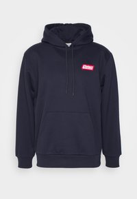 Sudadera azul marino con bolsillo frontal, capucha con cordón y parche del logo de Carhartt Service en rojo en el lado izquierdo del pecho.