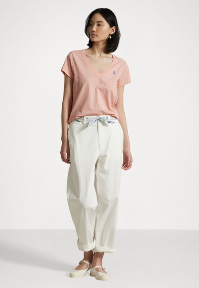 Pink cotton V-neck t-shirt with short sleeves, paired with white, loose-fitting, rolled-cuff trousers and light-colored espadrille shoes.
