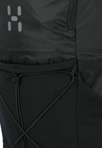 Bolsita de utilidad negra hecha de tejido texturizado que presenta un patrón de cuadrícula, detalle de cordón elástico y un logo sutil en gris claro.