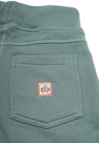 Gröna bomullsjoggers med ribbad midja, en bakficka med en rektangulär vävd etikett och kontrasterande sömnadsdetaljer.