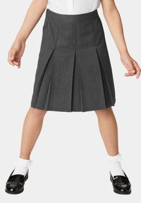 Grijze geplooide rok met een platte tailleband. De stof is soepel en licht. Gestyled met zwarte lakleren schoenen en witte gerimpelde enkelsokken.