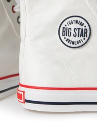 Las zapatillas altas de lona blanca tienen un logotipo redondo en azul y blanco que dice "BIG STAR" en el lateral. Acentos rojos y marinos en la suela.