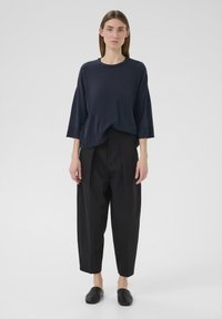 Übergroßes navyfarbenes Strickoberteil mit Dreiviertelärmeln, kombiniert mit schwarzen, hoch taillierten schmalen Hosen und schwarzen Slippern.
