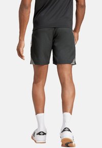 Pantaloncini atletici neri con finitura testurizzata, caratterizzati da pannelli laterali grigi. Indossati con calzini bianchi e scarpe da ginnastica nere con suola in gomma.