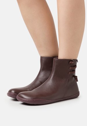 Bottes cheville en cuir marron à texture lisse, bout arrondi et trois boucles décoratives sur le côté. Semelle en caoutchouc plate, design minimaliste.