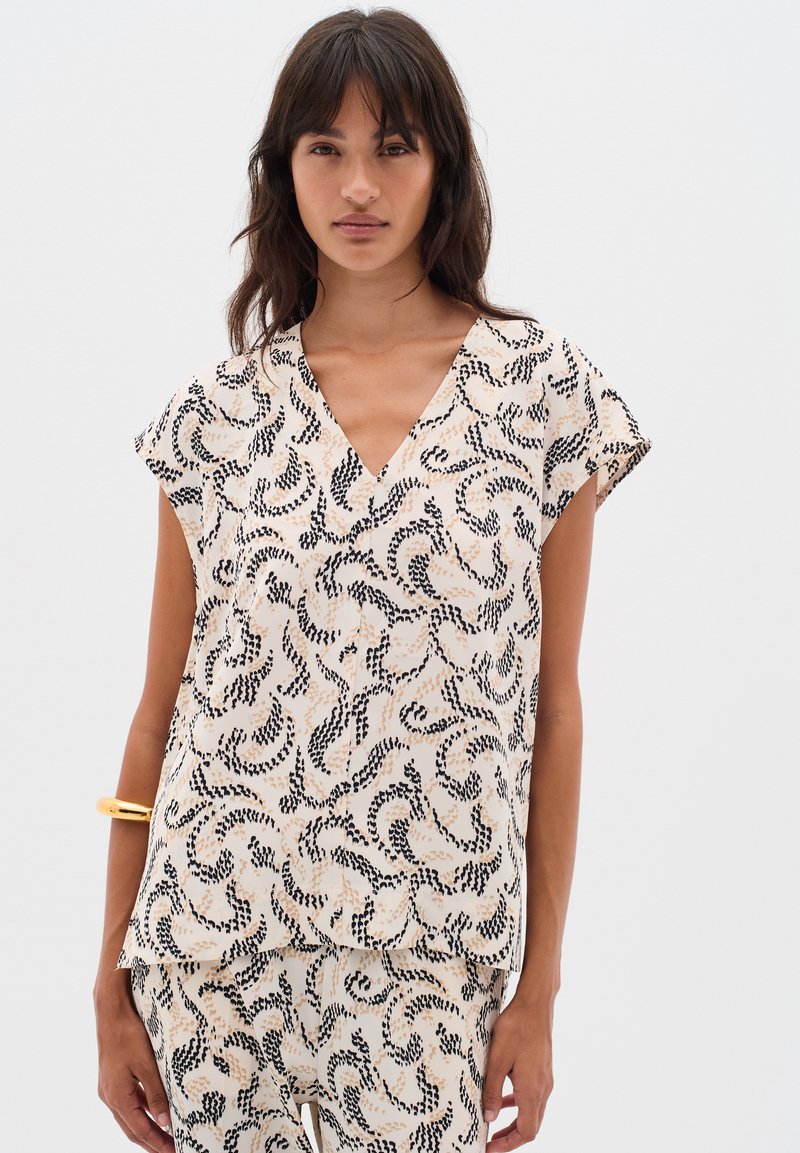 Blusa a maniche corte in tessuto crema con un motivo vorticoso nero e beige. Design a V con una vestibilità comoda. Texture liscia.