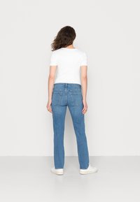 Jeans de denim azul claro com um corte reto, dois bolsos traseiros e uma cintura média, combinados com uma t-shirt branca ajustada.