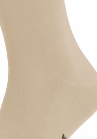 Calcetín crew beige hecho de un tejido texturizado, con un diseño acanalado y un acento de logo negro cerca del dedo del pie. Forma suave y ajustada.