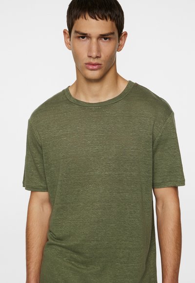 T-shirt à manches courtes couleur olive en tissu léger et texturé. Il est doté d'un col rond et d'une coupe décontractée.