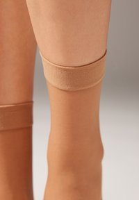 Medias hasta la rodilla beige translúcidas con una textura suave, que cuentan con suaves bandas elásticas en la parte superior para un ajuste seguro y comodidad.