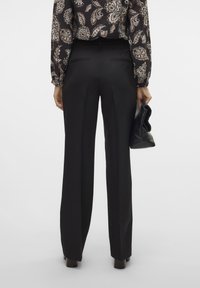 Zwarte op maat gemaakte broek met een rechte pijpontwerp, gekenmerkt door een soepele textuur en twee achterzakken, gecombineerd met een zwarte clutch.