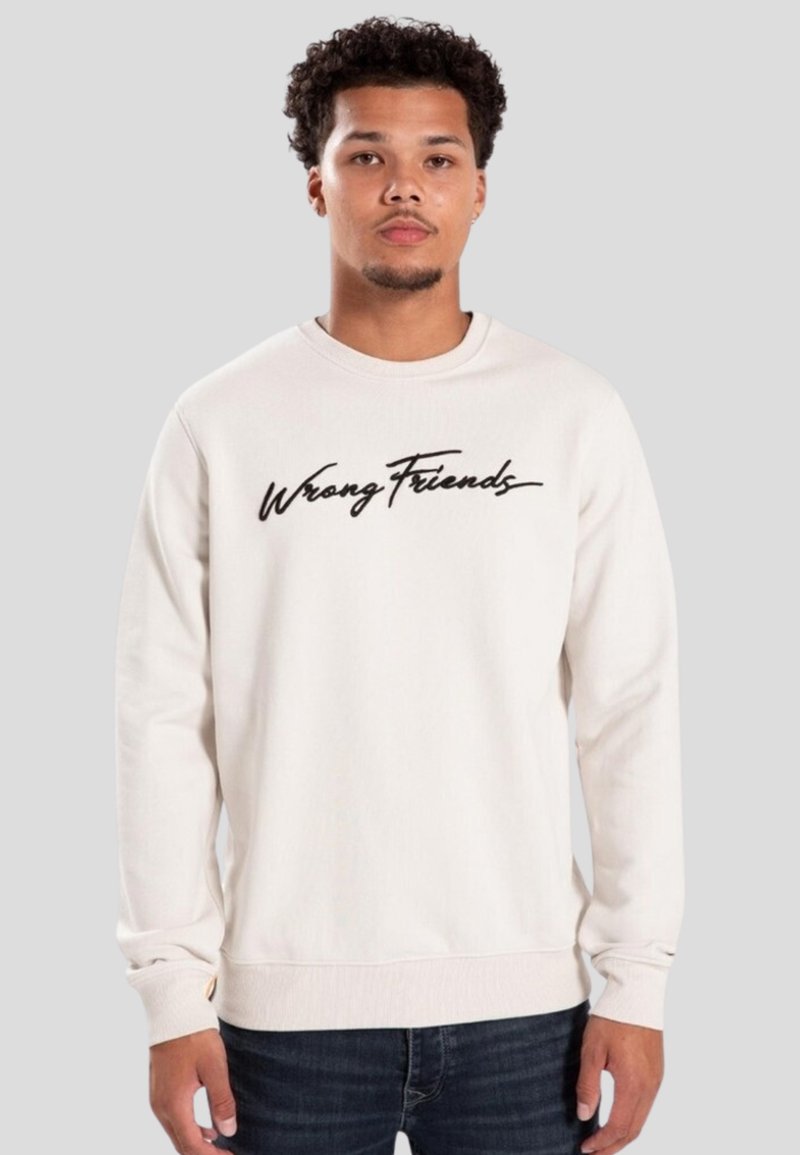 Felpa leggera beige con maniche lunghe e polsini a costine. Presenta la scritta in corsivo nero "Wrong Friends" sul petto. Materiale in cotone.