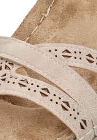 Sandalia beige con recortes decorativos y acentos de costura. Hecha de un material suave parecido al ante, con tiras superpuestas que presentan patrones triangulares.