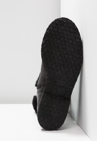 Semelle de botte noire avec motif de bande de roulement texturé circulaire, montrant partiellement une fermeture éclair et une doublure en fourrure sur le côté, sur fond blanc.
