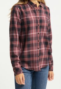 Skjorta med knäppning som har ett röd- och svartrutig mönster, lång ärm, krage och svarta knappar. Bärs tillsammans med blå denimjeans.