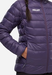 Doudoune violette en tissu lisse et isolé avec des coutures horizontales, une fermeture éclair à l'avant et une poche latérale discrète. Logo de la marque sur la poitrine.