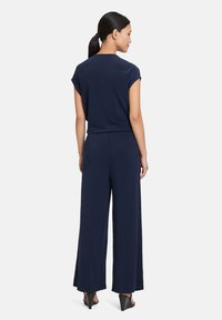 Navy jumpsuit with short sleeves and wide-leg trousers, featuring a soft, textured fabric and a back zipper detail for easy wear.