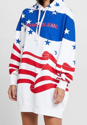 Sudadera con capucha extragrande con diseño de la bandera estadounidense, estrellas azules sobre fondo blanco en la parte superior, franjas rojas y blancas abajo, y texto "Calvin Klein Jeans".