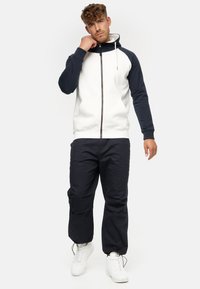 Sudadera con capucha de frontal blanco y mangas azul marino, con cremallera completa, cordones y bolsillos tipo canguro, combinada con pantalones azul marino.