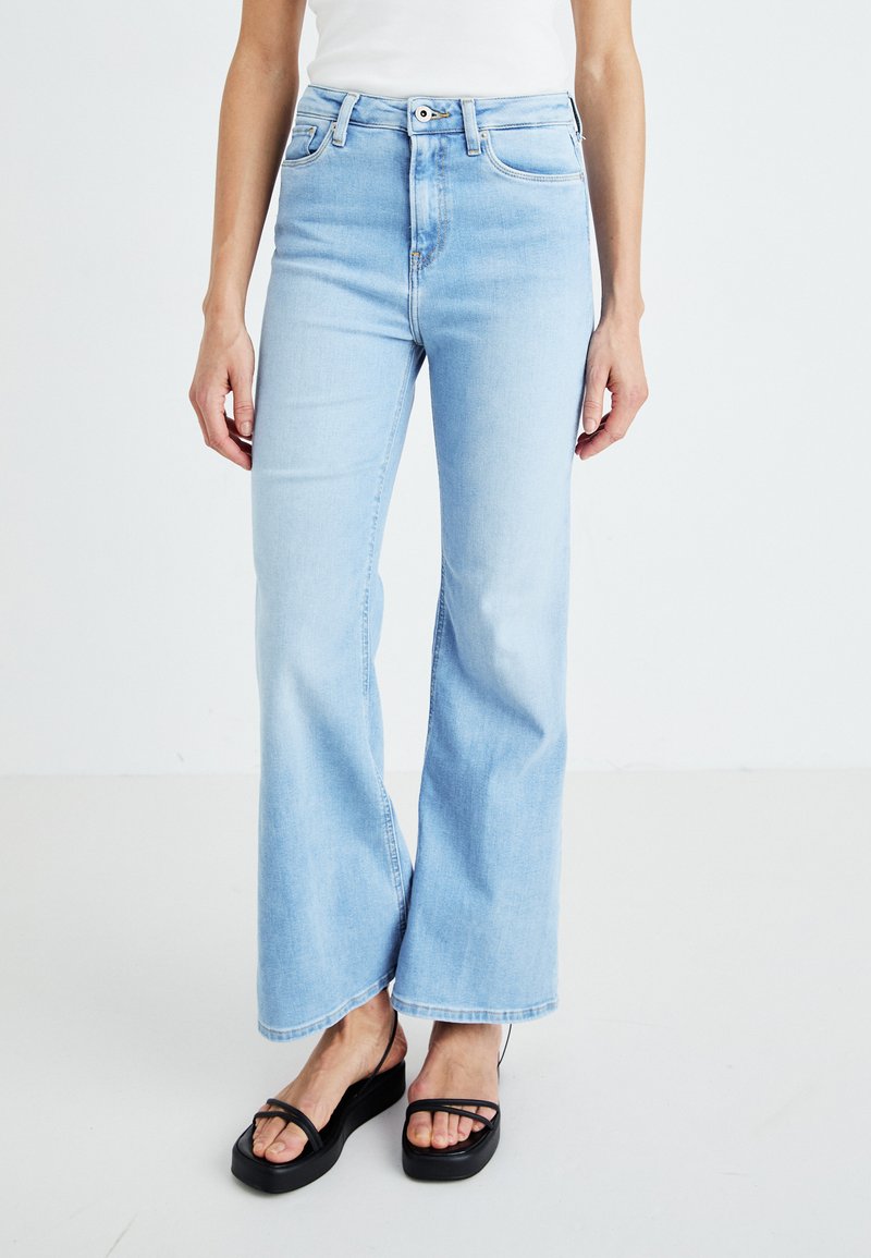 Høyt midje lys blå denimbukser med vid ben design, med fem lommer og knappelukking, sammen med svarte platåsandaler.