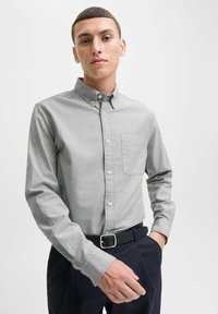 Camicia grigia con bottoni, taschino sul petto, maniche lunghe, colletto piccolo e texture liscia, abbinata a pantaloni blu navy e una cintura nera.