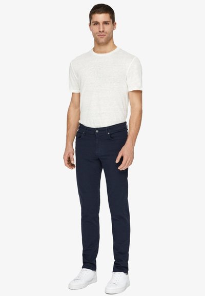 Blugi slim-fit de culoare bleumarin, cu buzunare standard, asortați cu un tricou cu guler rotund texturat de culoare deschisă și adidași albi.