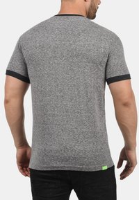 Camiseta gris de manga corta con ribete negro en el cuello y las mangas, que presenta una tela texturizada y una pequeña etiqueta de acento verde en la parte inferior.