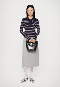 Marineblau und rosa gestreiftes Langarm-Polohemd, grauer Rock mit Spitzenkante, schwarze Lackhandtasche, silberne spitze Pumps, weiße Socken.