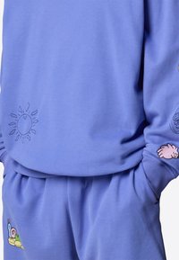 Sudadera púrpura y pantalones a juego, con bordados de un sol, un caracol y diseños de manos. Tejido suave con puños y cinturilla acanalados.