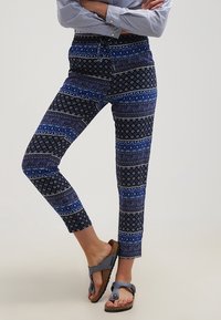 Blå mönstrade byxor med en blandning av ränder och blommönster, med resår i midjan och kort längd. Kombinerade med svarta sandaler.