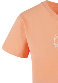 Lys rosa t-skjorte med korte ermer laget av bomull. Har V-hals og en liten brodert hvit logo på brystområdet.