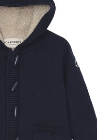 Cardigan con cappuccio in maglia blu navy, foderato in morbido pile beige, con grandi bottoni di chiusura e due tasche frontali. Presenta una toppa con il logo sulla manica.