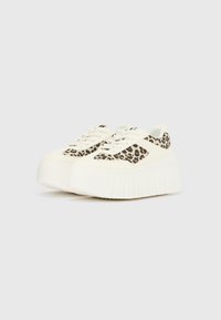 Baltas platformas sporta kurpes ar reljefu zoli, sānos ar leoparda raksta paneļiem un tradicionālu mežģīņu aizdari.