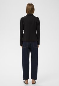 Fekete blézer strukturált kialakítással, formázott vállakkal és peplum derékkal. Lazább sötét farmernadrággal párosítva, kiemelt hátsó zsebekkel.