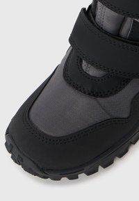 Bottin de randonnée noir et gris avec des sangles Velcro, tige en tissu texturé, semelle extérieure en caoutchouc et bout renforcé pour la durabilité et l'adhérence.