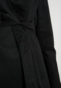 Mustapukuinen takki, jossa on tekstuuri, edessä solmittava vyö ja sivutaskut. Sopii erilaisiin tyyleihin ja tilaisuuksiin.