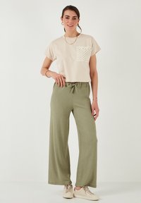 Beige cropped t-shirt met gestructureerde zak; olijfgroene wijde broek met elastische taille; beige sneakers. Glad katoen textuur.