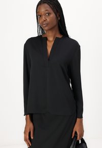 Maglietta nera a maniche lunghe realizzata in tessuto morbido; presenta un neckline a V e una vestibilità comoda. Il design è semplice, senza pattern o dettagli.