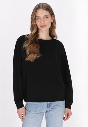 Musta puuvillane sweatshirt ümmarguse kaelusega, langenud õlgade ja pikkade varrukatega, koos helesiniste teksadega, et saavutada mugav sobivus.