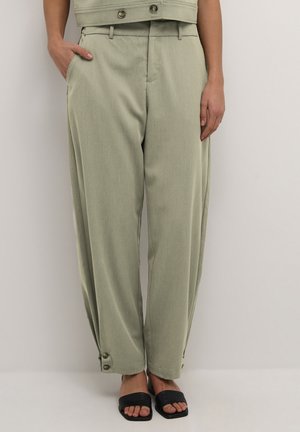 Hellgrüne, schmal zulaufende Hose mit Seitentaschen, einem Knopfdetail am Saum und einem glatten Stoffgefühl. Getragen mit schwarzen Riemchensandalen.