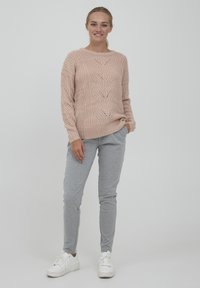 Maglione lavorato a maglia di un leggero rosa con un motivo a treccia testurizzato, abbinato a pantaloni della tuta grigi e sneakers bianche. Vestibilità casual e rilassata.