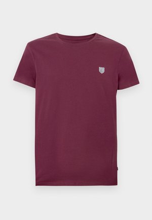 Tricou din bumbac burgundy, cu guler rotund și mâneci scurte. Prezintă un mic logo în formă de scut în partea stângă sus a pieptului. Textură netedă.