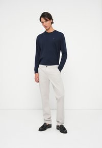 Cămașă cu mânecă lungă de marină, pantaloni bej deschis șiloaferi negri. Croială slim, textură fină și design minimalist fără modele proeminente.