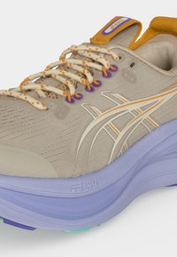 Μπεζ και πορτοκαλί παπούτσι για τρέξιμο Asics με λευκά και πορτοκαλί κορδόνια, μοβ τρύπες για κορδόνια και χοντρή ανοιχτό μοβ σόλα με την ένδειξη FF Blast+